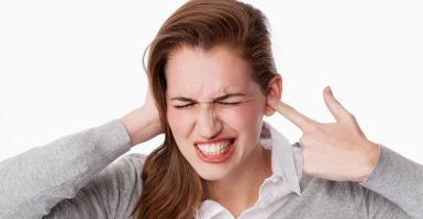 tinnitus concept - enraged young woman having painful headache,covering closed ears,annoyed by loud noise not wanting to hear their side of story